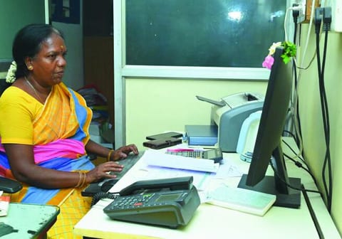 A woman at an office desk typing at a computer, with a desk phone and a printer beside her.