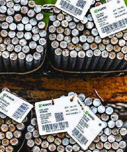 White printed tags with a barcode and QR code hung on the cut ends of bundled steel bars.