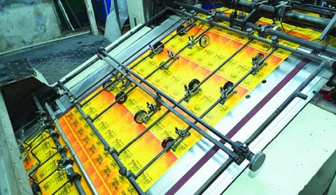 Sheets of printed yellow and orange tags running through a printing press.
