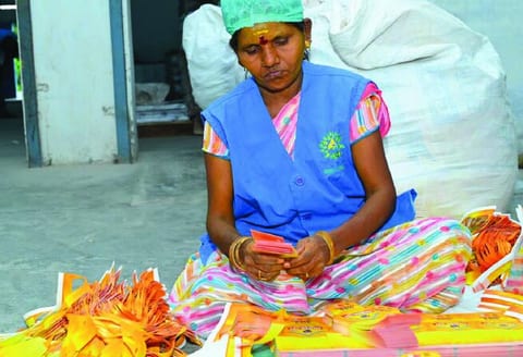 A woman seated on the floor sorting printed tags by hand.