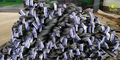Coils of steel bars in an outdoor yard, each wrapped with a blue and white stick-on tag