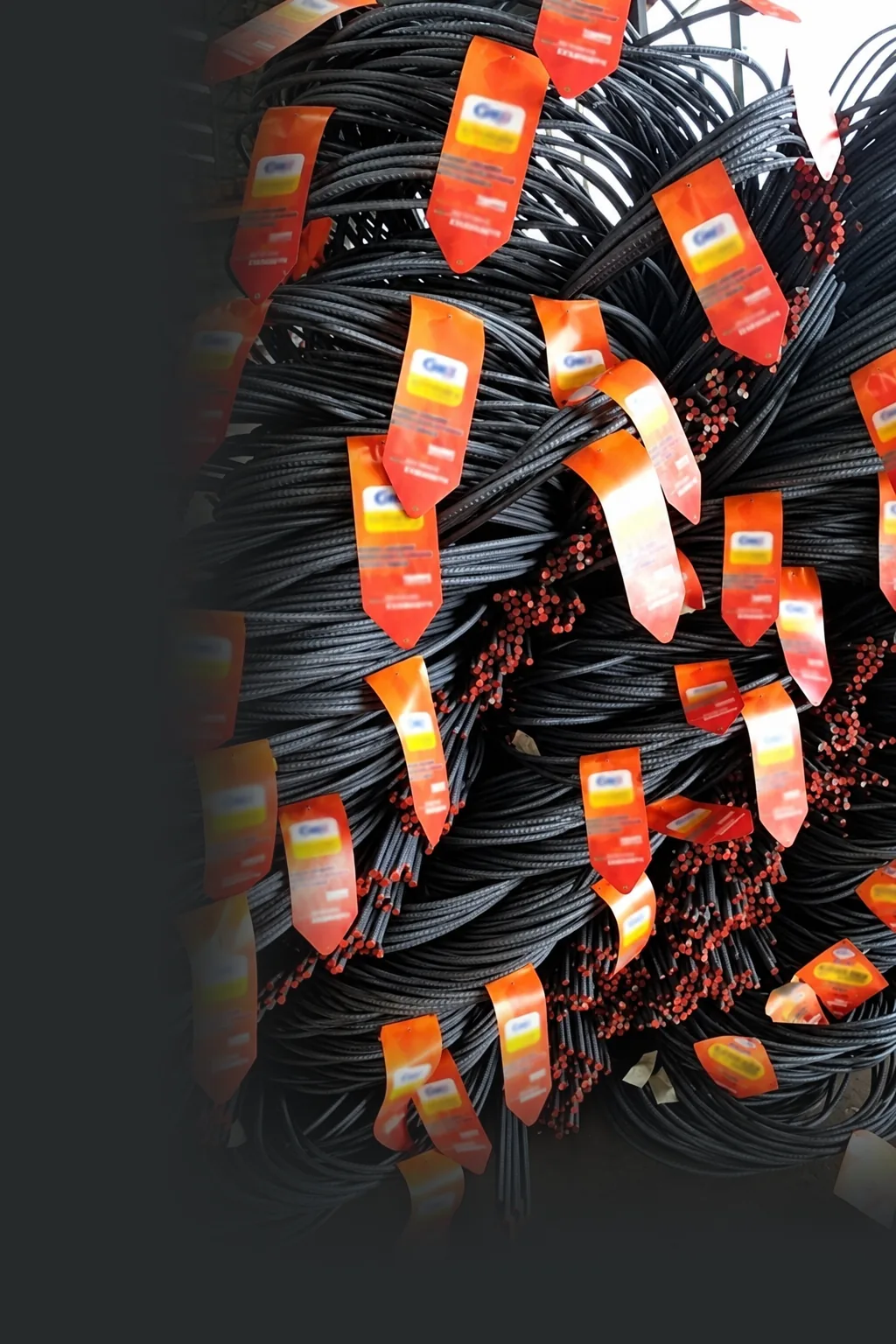 Coils of steel bars in a warehouse, each carrying a bright orange printed tag